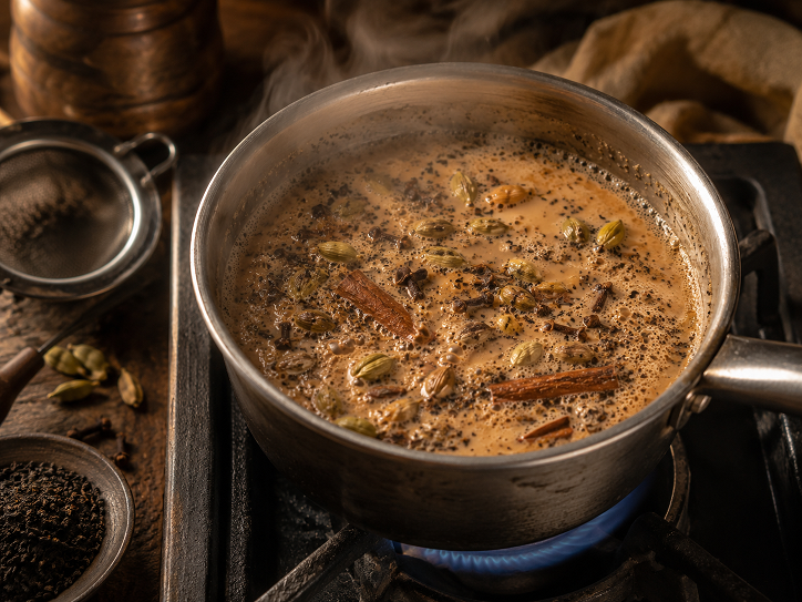 Loose leaf masala chai being brewed on a stovetop in a small saucepan with milk and spices